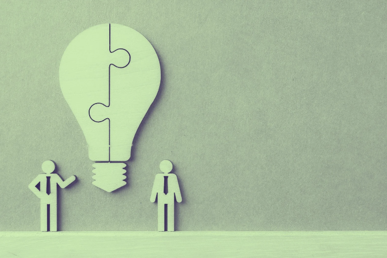 Abstract silhouettes beside a puzzle-piece lightbulb symbolizing teamwork and creative problem-solving.